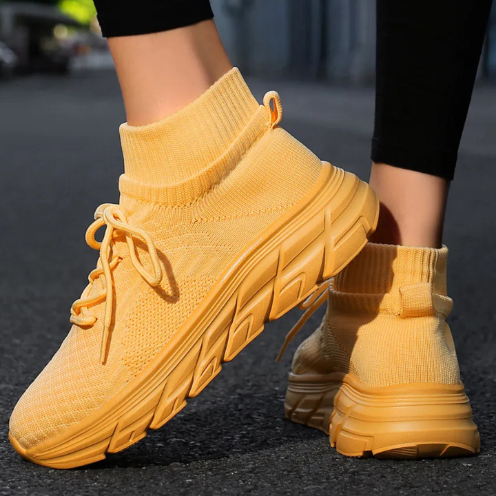 Gele sneakers met dikke zool, gebreid bovenwerk en veters, gedragen op asfalt. Trendy sportschoenen voor dames, comfortabele en modieuze stijl.