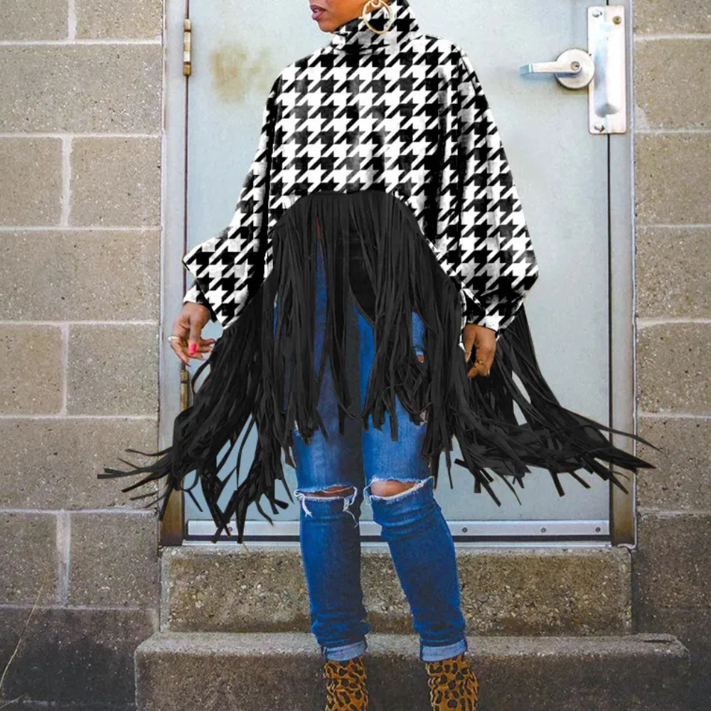Damesmode: Zwart-witte pied-de-poule poncho met franjes, gecombineerd met gescheurde jeans en luipaardprint laarzen. Trendy herfstoutfit.