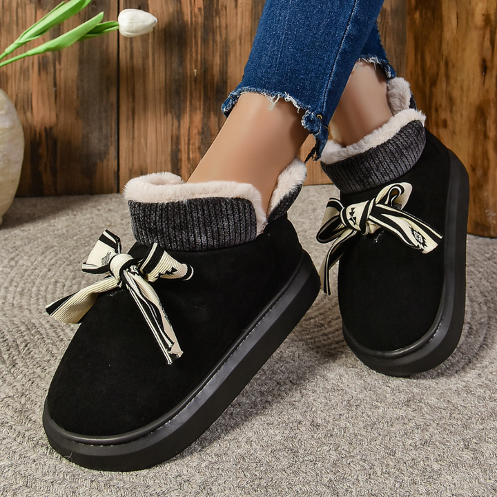 Zwarte damespantoffels met strik, warme voering en dikke zool, perfect voor wintercomfort. Stijlvolle en comfortabele huisschoenen voor dames.