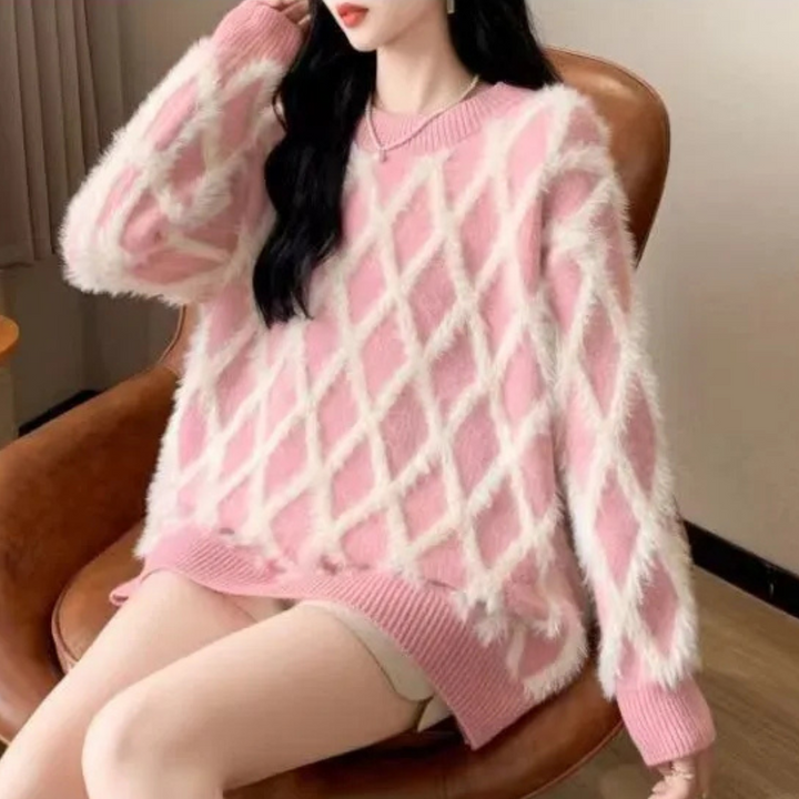 Dame in roze gebreide trui met ruitpatroon, zittend op bruine stoel. Modieuze winterkleding, comfortabele en stijlvolle damestrui.