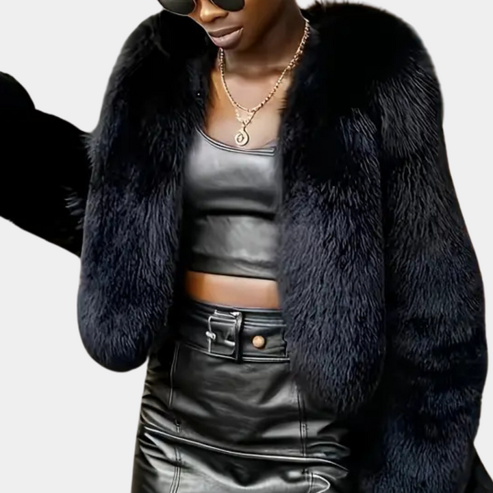 Vrouw in zwarte nepbontjas, leren crop top en rok, met zonnebril en ketting. Modieuze winterkleding, trendy damesmode, luxe uitstraling.
