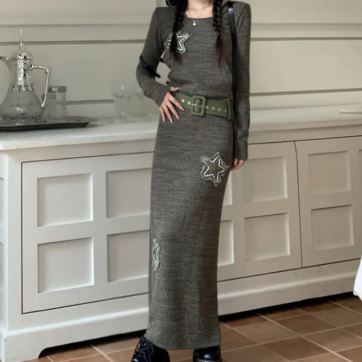 Grijze gebreide maxi-jurk met sterapplicaties, brede riem en zwarte laarzen. Trendy damesmode, herfst-winter outfit, stijlvolle kleding.