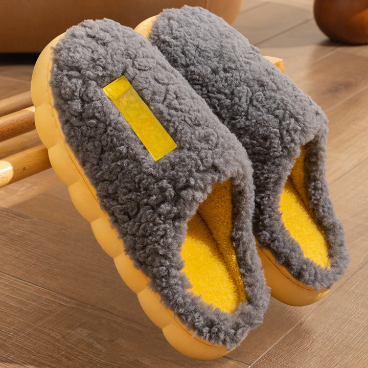 Grijze pluche pantoffels met gele binnenvoering op houten vloer. Comfortabele, warme huisschoenen voor winterse dagen. Perfect voor thuisgebruik.