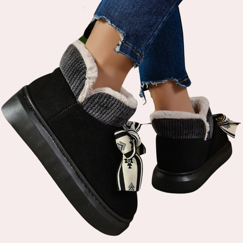 Zwarte dameslaarzen met bontvoering en decoratieve strik, gedragen met gescheurde jeans. Comfortabele wintermode, warme schoenen voor dames.