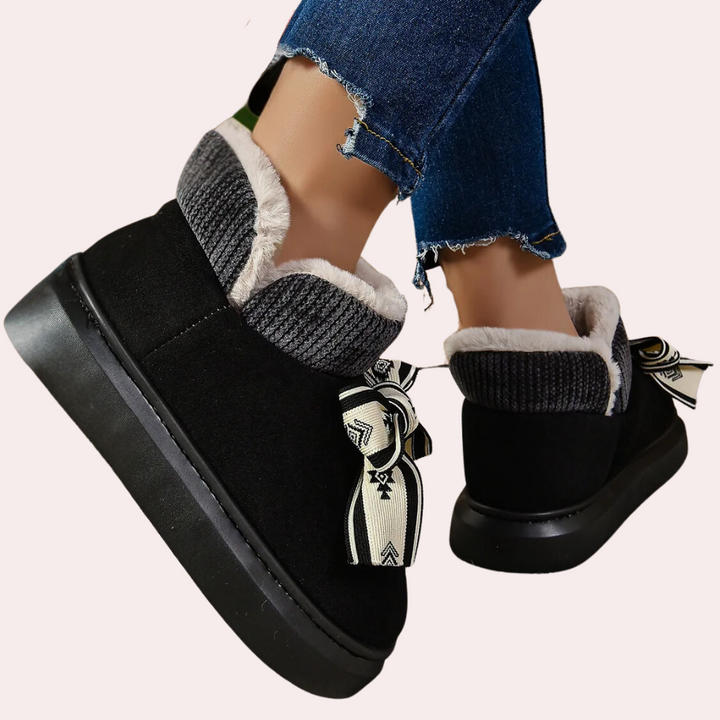 Zwarte dameslaarzen met bontvoering en decoratieve strik, gedragen met gescheurde jeans. Comfortabele wintermode, warme schoenen voor dames.