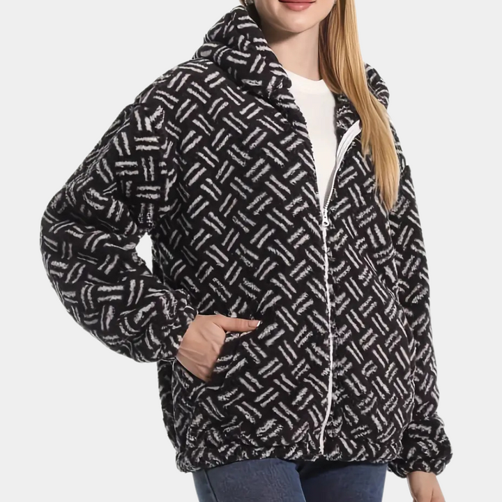 Vrouw draagt een zwart-witte fleecejas met geometrisch patroon, ritssluiting en zakken. Modieuze winterkleding, comfortabele damesjas.