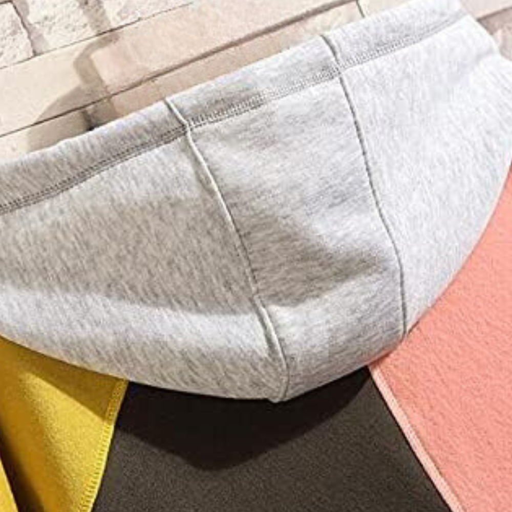 Grijze capuchon van een kleurrijke hoodie met roze, gele en bruine vlakken, tegen een bakstenen achtergrond. Modieuze streetwear stijl.