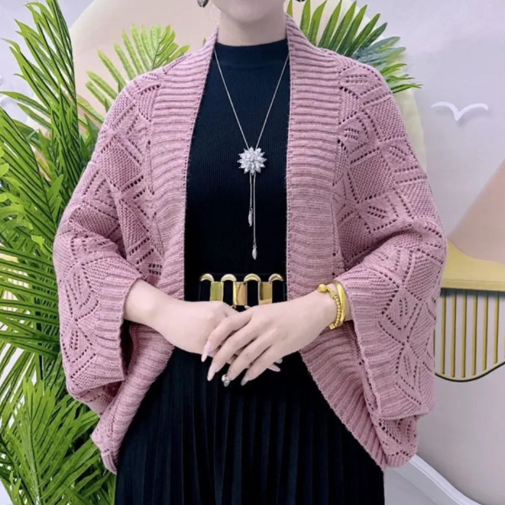 Vrouw draagt roze gebreid vest met geometrisch patroon, zwarte jurk en gouden accessoires. Stijlvolle mode, herfstkleding, damesoutfit.