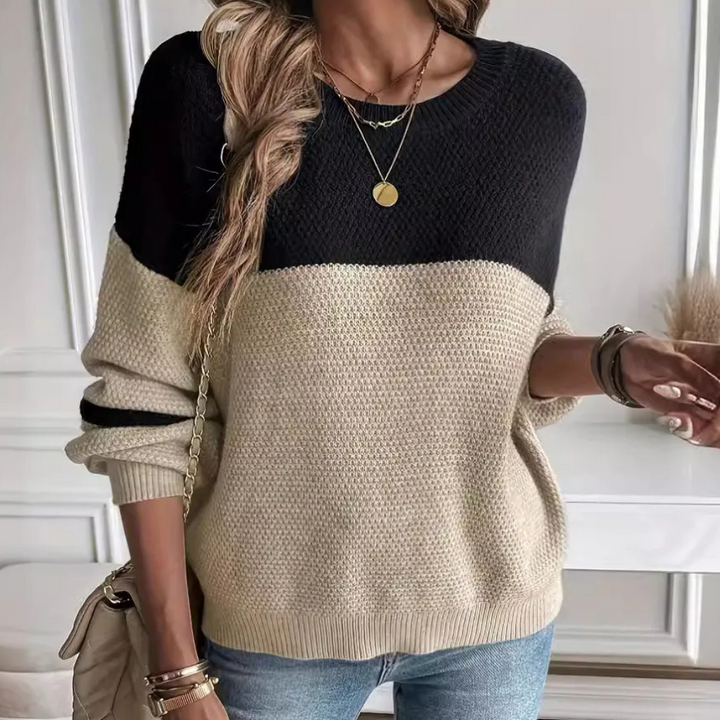Vrouw draagt stijlvolle zwart-beige trui met ronde hals, gecombineerd met blauwe jeans en gouden sieraden. Perfecte herfstmode voor casual look.