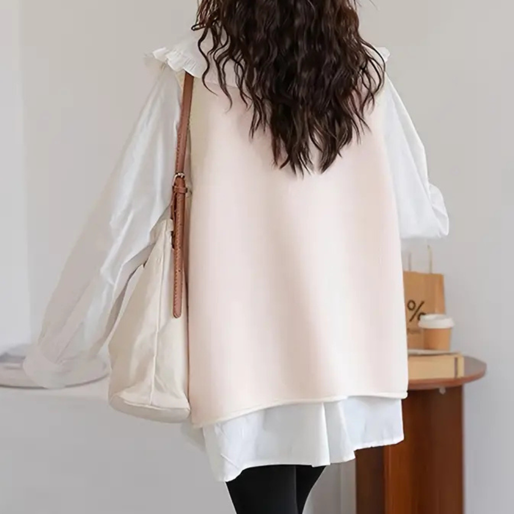 Vrouw in witte blouse en beige vest, draagt een canvas tas. Modieuze herfstoutfit, casual stijl, geschikt voor dagelijks gebruik.