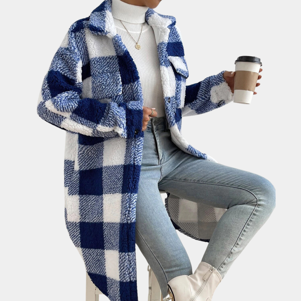 Vrouw in blauwe geruite jas, witte coltrui en jeans, zittend met koffiebeker. Modieuze winteroutfit, casual stijl.