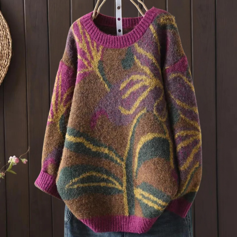 Bruine oversized trui met kleurrijk bloemenpatroon, ronde hals en lange mouwen, hangend voor een houten achtergrond. Perfect voor herfstmode.