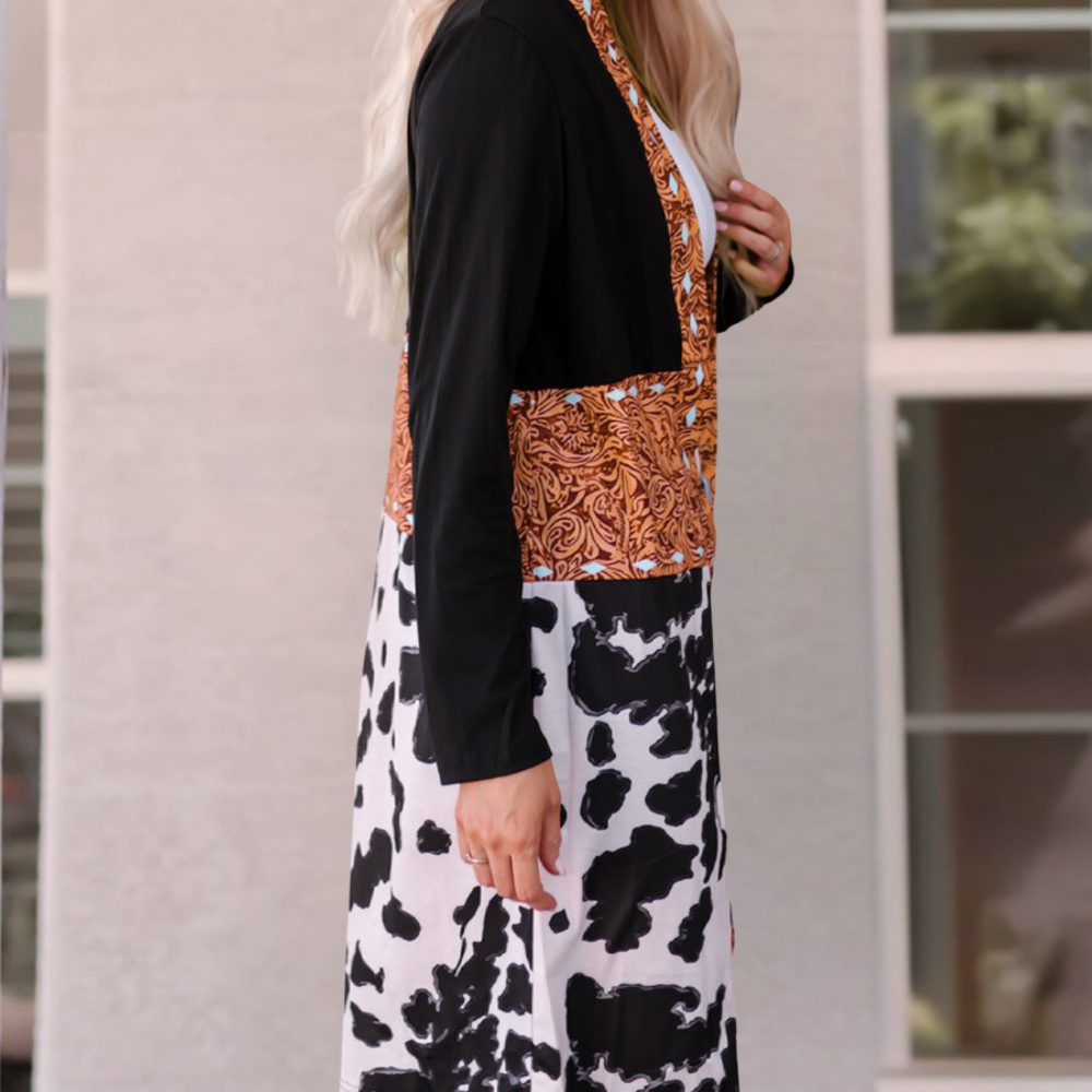 Vrouw in modieuze jurk met koeienprint en oranje patroon, staand voor een moderne achtergrond. Trendy damesmode, unieke kledingstijl.