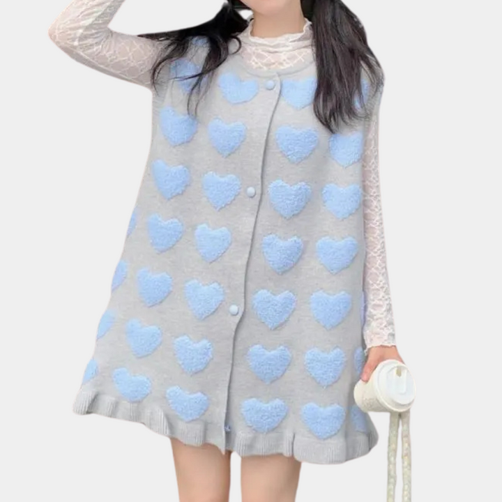 Grijze mouwloze jurk met blauwe hartjes, gedragen door vrouw met witte kanten top. Trendy damesmode, casual stijl, romantisch design.