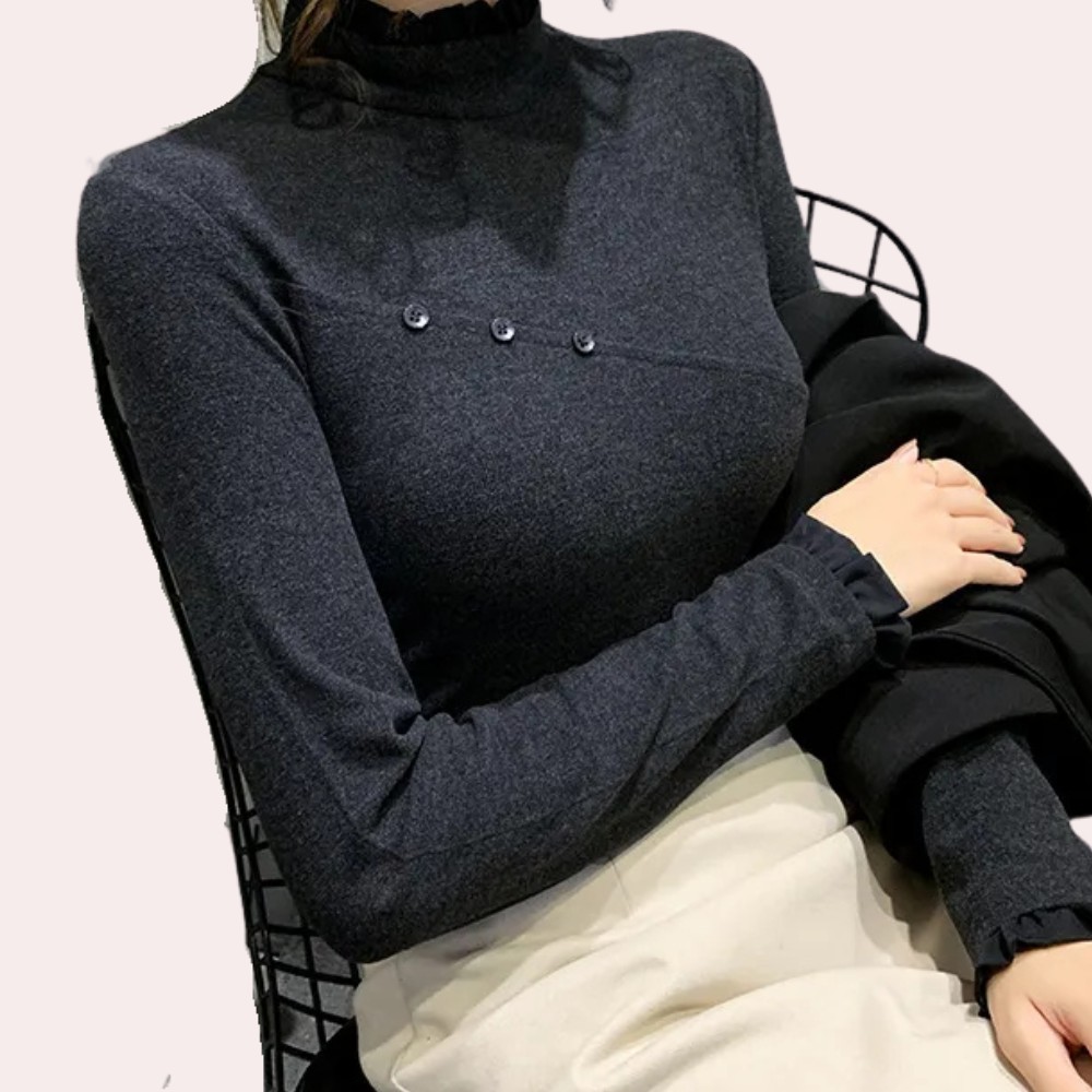 Donkergrijze damestrui met hoge kraag en knoopdetails, gedragen door model op zwarte stoel. Stijlvolle herfstmode, comfortabele pasvorm.