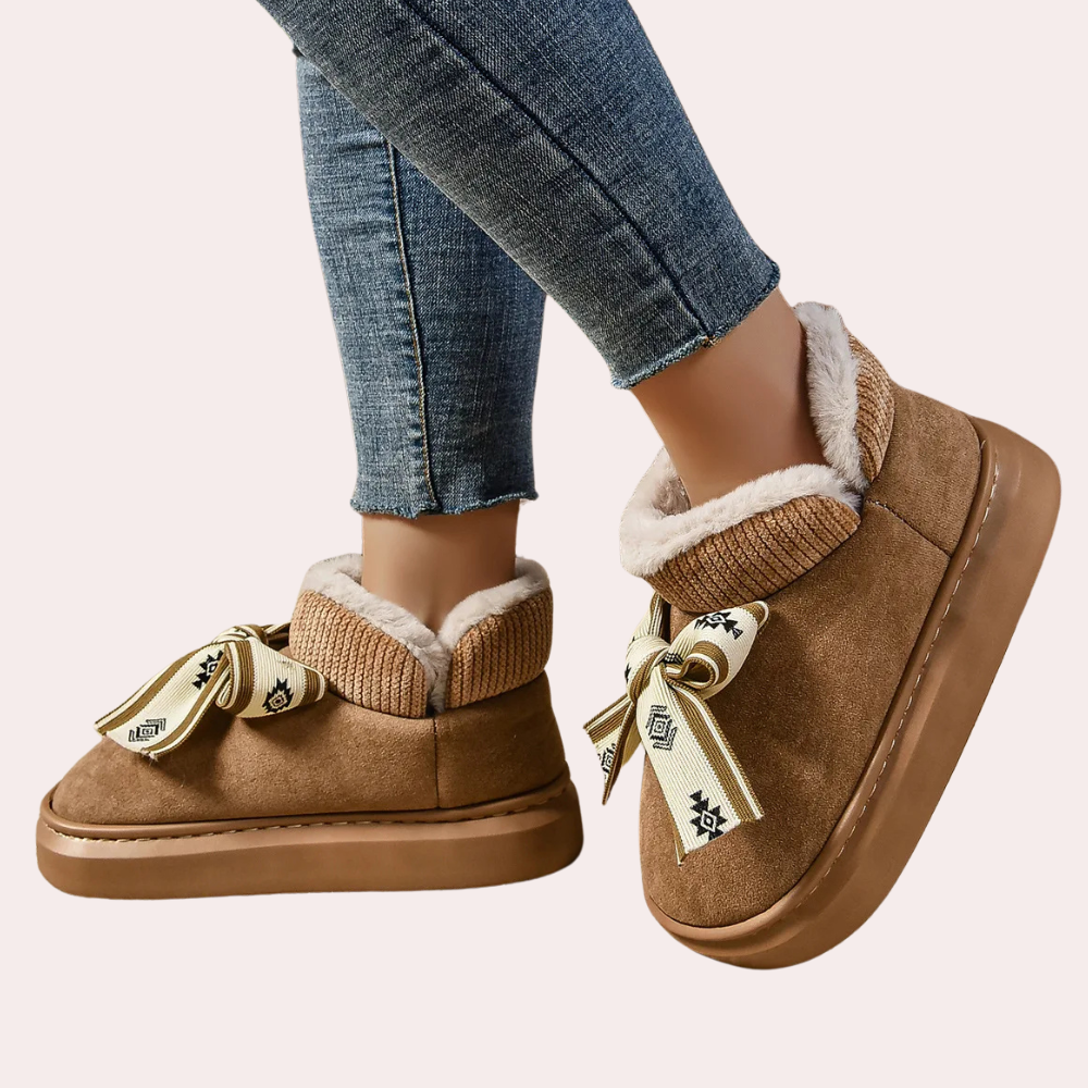 Bruine suède enkellaarsjes met bontvoering en decoratieve strik, gedragen met blauwe jeans. Comfortabele wintermode, warme dameslaarzen.