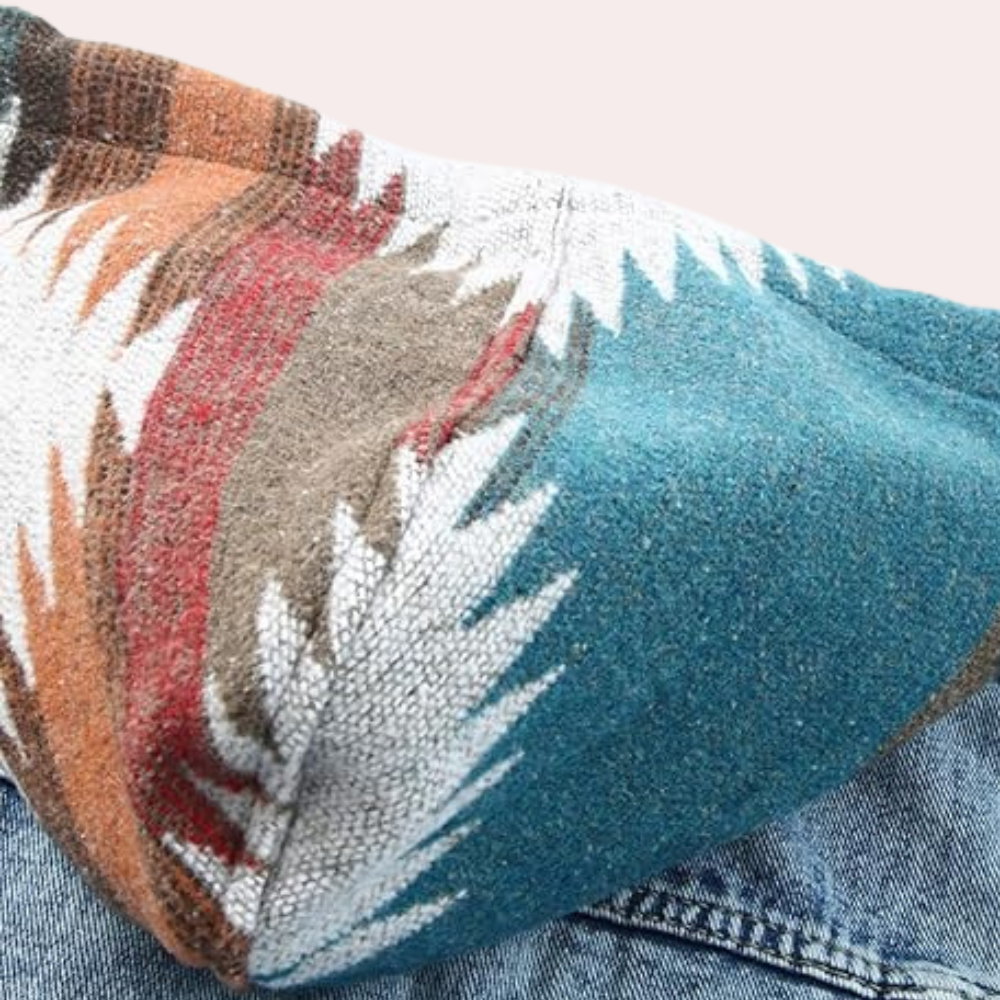 Gebreide trui met kleurrijk Azteeks patroon, turquoise, rood en bruin, op een spijkerbroek. Modieuze herenkleding, herfst/winter stijl.
