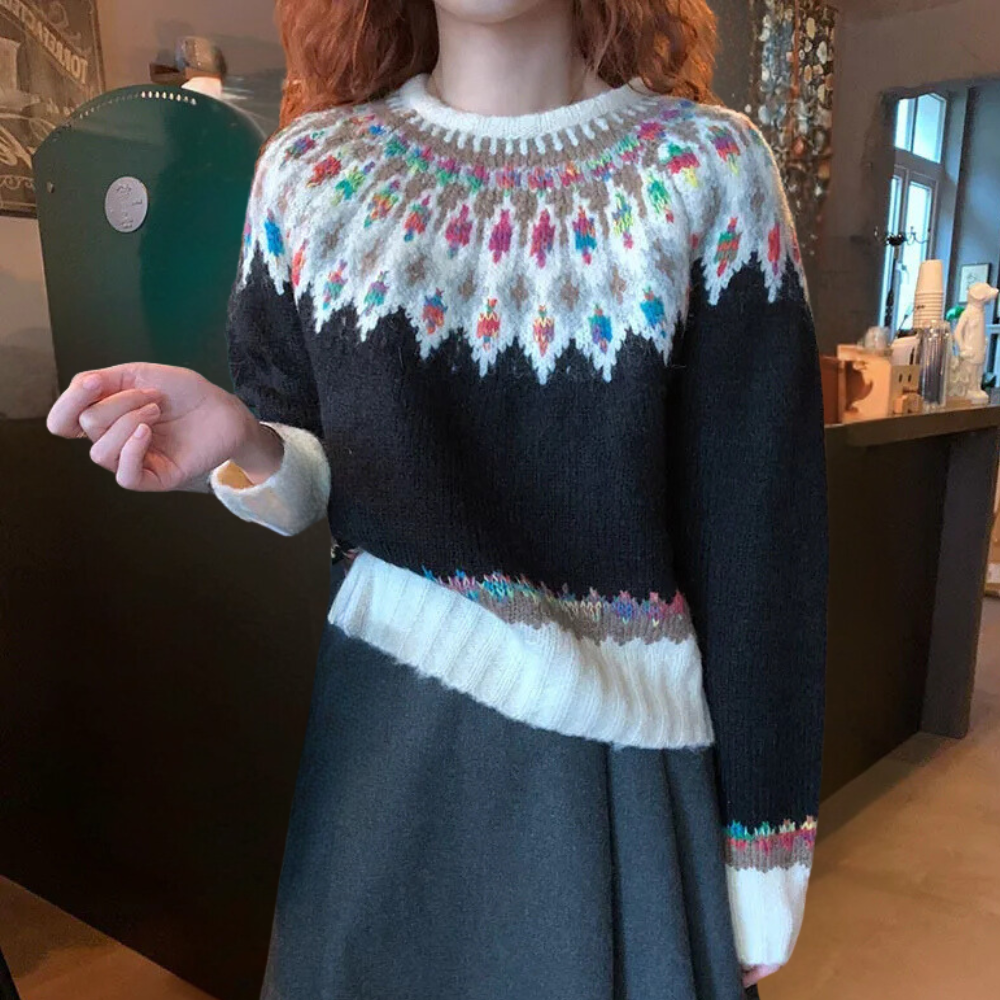 Vrouw draagt een zwarte trui met kleurrijk Noors breipatroon, ideaal voor wintermode. Stijlvolle, warme dameskleding in een gezellige omgeving.