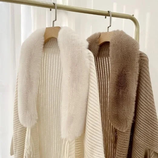 Twee gebreide vesten met luxe bontkragen, wit en beige, hangend aan een kledingrek. Stijlvolle wintermode, warme dameskleding.