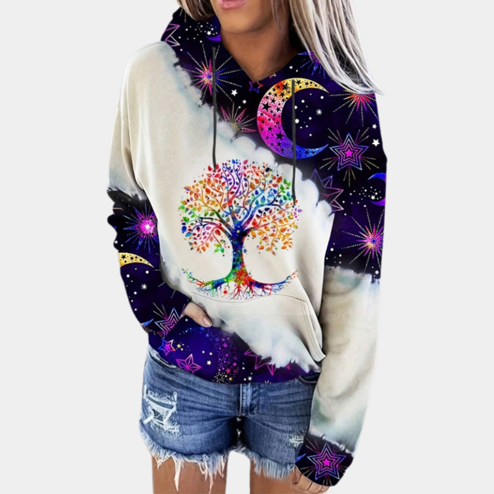 Vrouw draagt kleurrijke hoodie met levensboom en sterrenprint, gecombineerd met denim shorts. Trendy mode, casual streetwear, unieke ontwerpen.