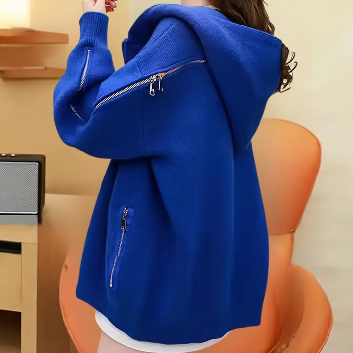 Blauwe oversized hoodie met ritsen, gedragen door een persoon, zittend op een oranje stoel. Modieuze dameskleding, comfortabele casual stijl.