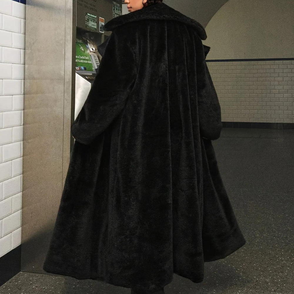 Zwarte lange bontjas, gedragen door persoon in metrostation. Stijlvolle wintermode, luxe uitstraling, warme kleding, stedelijke achtergrond.