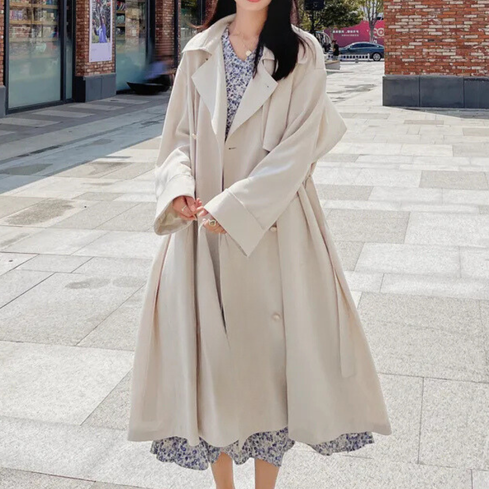 Vrouw in beige trenchcoat en bloemenjurk op straat, mode herfst 2023, stijlvolle dameskleding, stedelijke achtergrond.