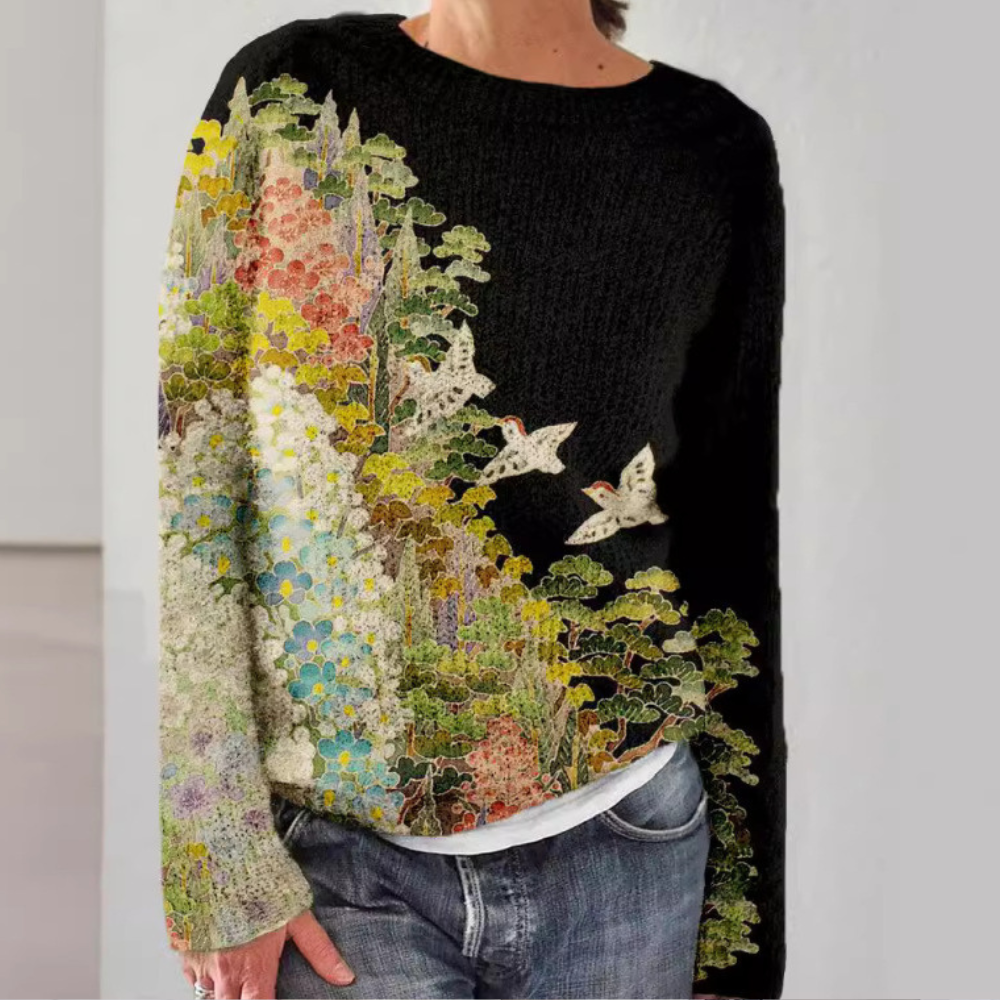 Vrouw draagt zwarte trui met kleurrijk bloemen- en vogelpatroon, casual jeans. Modieuze dameskleding, herfsttrui, unieke gebreide stijl.