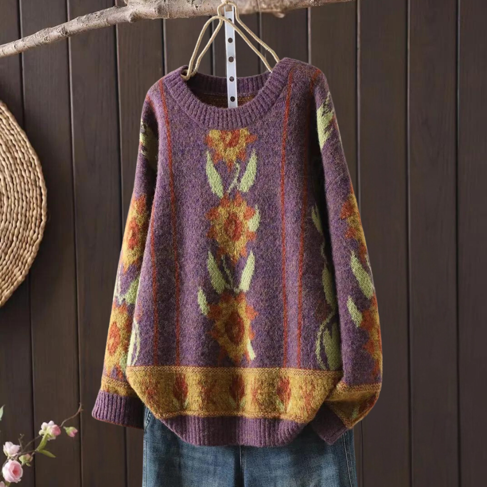 Paarse gebreide trui met bloemenpatroon, hangend aan houten hanger. Vintage damesmode, herfstkleding, kleurrijk design, warme wollen stof.