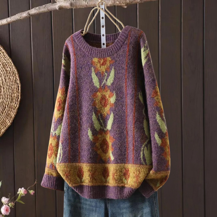 Paarse gebreide trui met bloemenpatroon, hangend aan houten hanger. Vintage damesmode, herfstkleding, kleurrijk design, warme wollen stof.