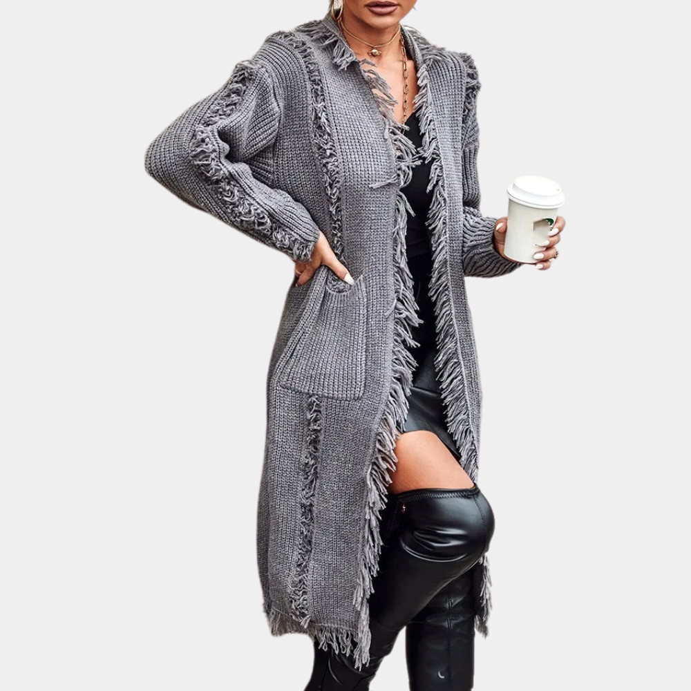 Grijze gebreide damesvest met franjes, lange mouwen en zakken, gedragen over een zwarte jurk. Perfect voor herfstmode en casual stijl.