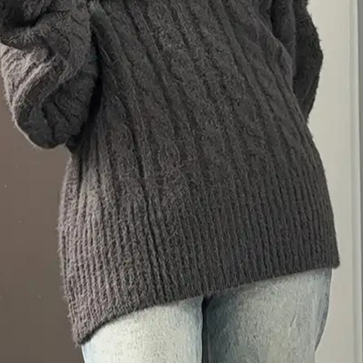 Grijze gebreide trui met kabelpatroon, gedragen door persoon in blauwe jeans. Comfortabele wintermode, casual stijl, warme kleding.
