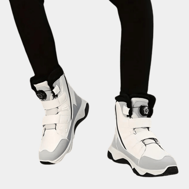 Witte snowboardschoenen met klittenbandsluiting en zwarte accenten, gedragen door persoon in zwarte broek. Ideaal voor wintersport en snowboarden.