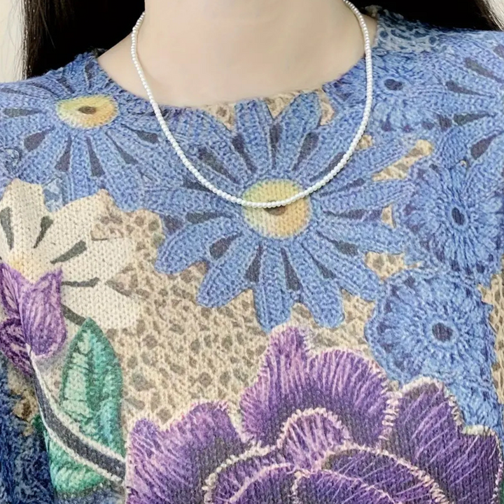 Vrouw draagt een zilveren ketting op een kleurrijke trui met bloemenprint. Modeaccessoires, dameskleding, trendy sieraden, bloemenpatroon.
