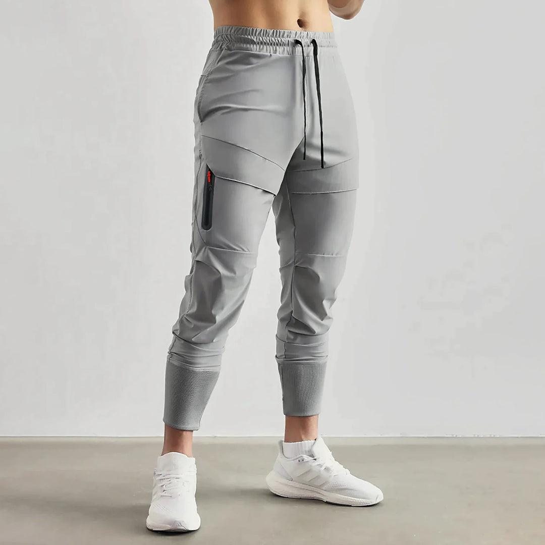 Grijze heren joggingbroek met elastische tailleband, zijzak met rits, en strakke enkelboorden. Comfortabele sportbroek voor dagelijks gebruik.