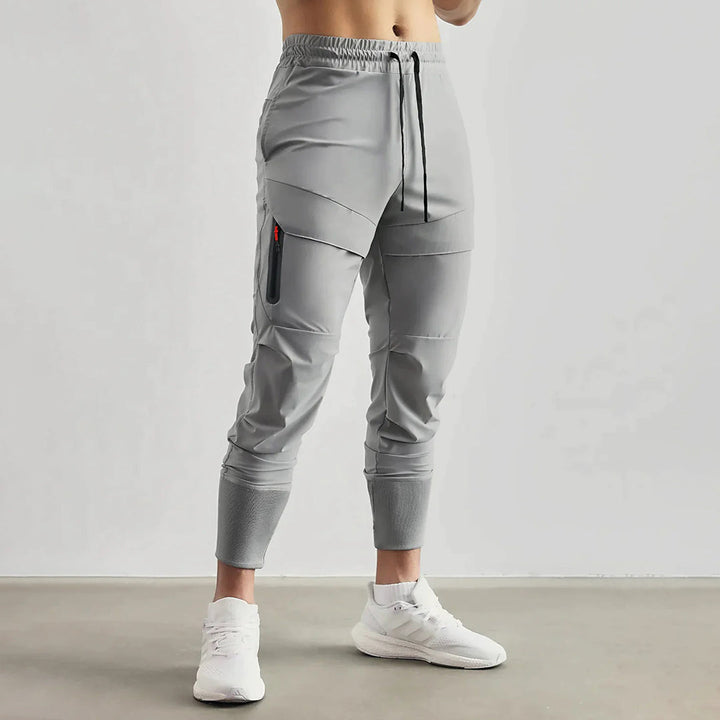 Grijze heren joggingbroek met elastische tailleband, zijzak met rits, en strakke enkelboorden. Comfortabele sportbroek voor dagelijks gebruik.
