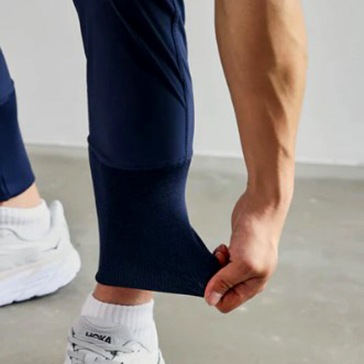 Man in donkerblauwe joggingbroek, trekt aan de enkelboord. Comfortabele sportkleding, herenmode, casual stijl, witte sneakers.