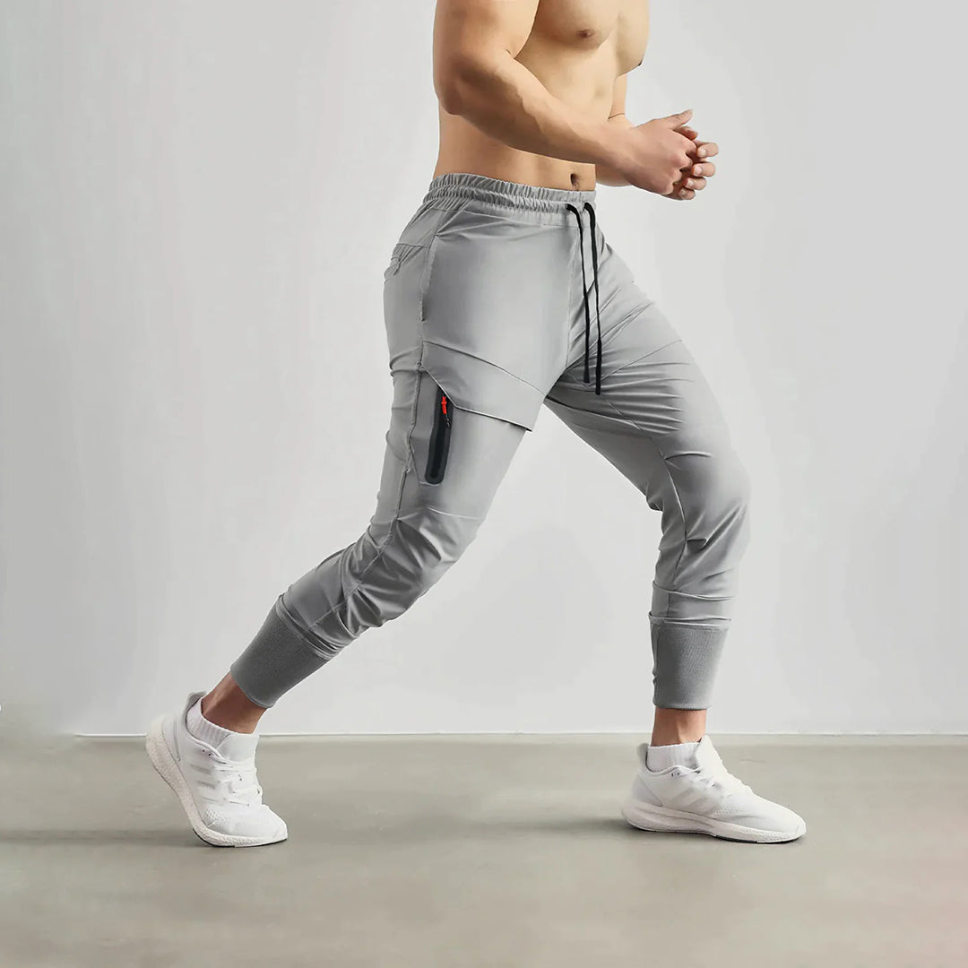 Grijze heren joggingbroek met zijzak, elastische tailleband en trekkoord, ideaal voor sport en casual gebruik. Comfortabele pasvorm, moderne stijl.