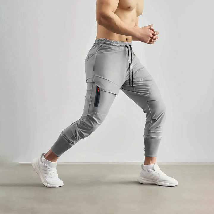 Grijze heren joggingbroek met zijzak, elastische tailleband en trekkoord, ideaal voor sport en casual gebruik. Comfortabele pasvorm, moderne stijl.