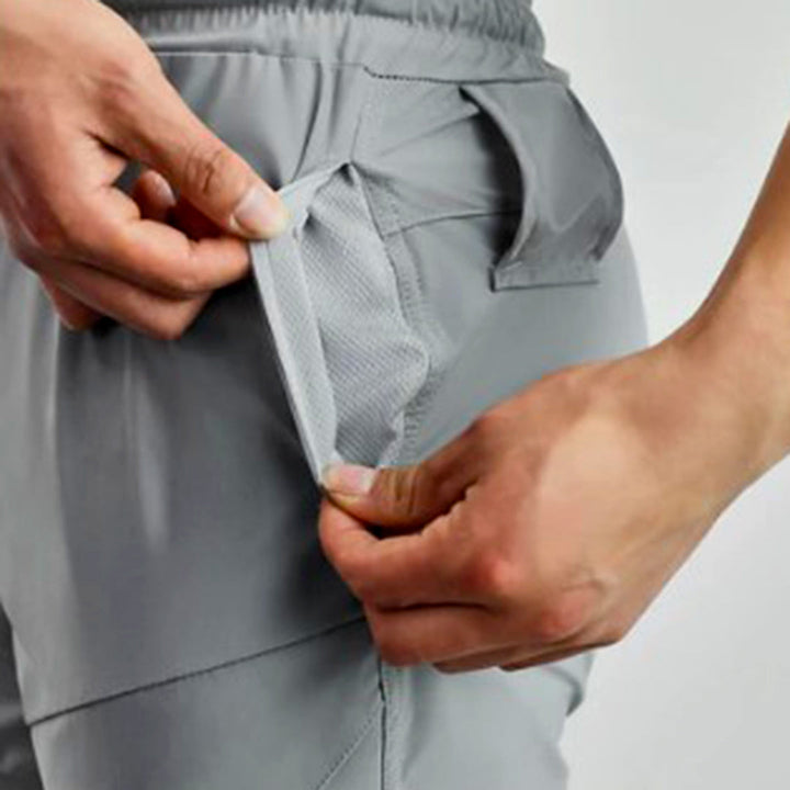 Grijze heren joggingbroek met elastische tailleband en zakken, close-up van hand die ritszak opent. Comfortabele sportkleding voor heren.