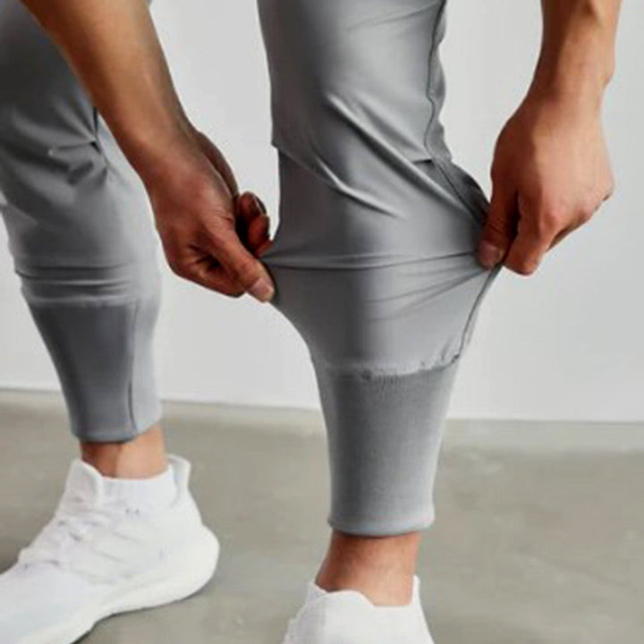Man in grijze joggingbroek, close-up van elastische stof, comfortabele pasvorm, sportkleding voor heren, casual stijl, witte sneakers.