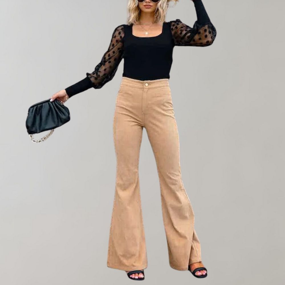 Vrouw in trendy corduroy uitlopende broek, zwarte top met doorschijnende mouwen, en zwarte tas. Modieuze dameskleding, herfstmode.