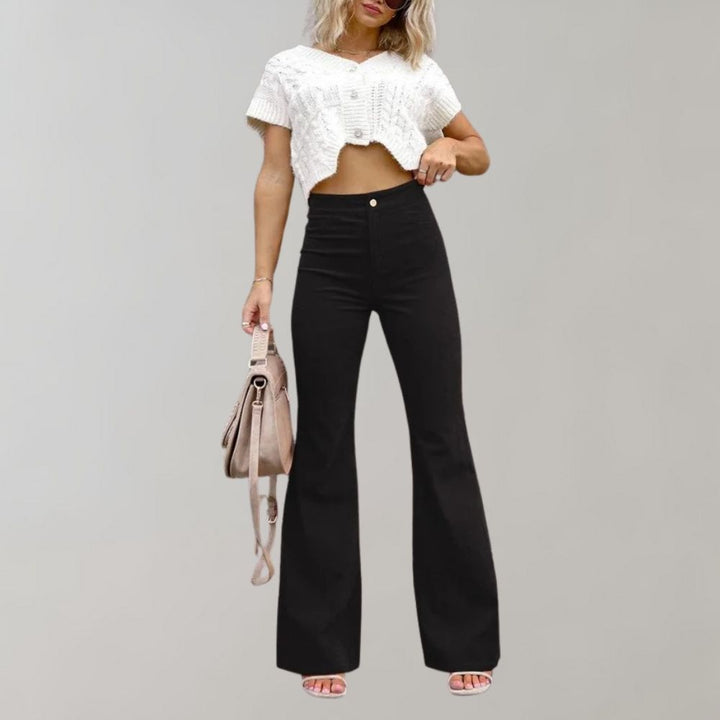 Vrouw in zwarte corduroy uitlopende broek en witte crop top, met beige handtas. Trendy damesmode, casual outfit, herfstkleding.