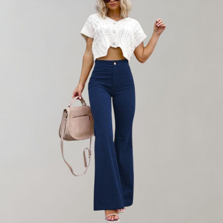 Vrouw in trendy donkerblauwe corduroy uitlopende broek, witte crop top en beige tas. Modieuze dameskleding, herfstmode, casual chic stijl.