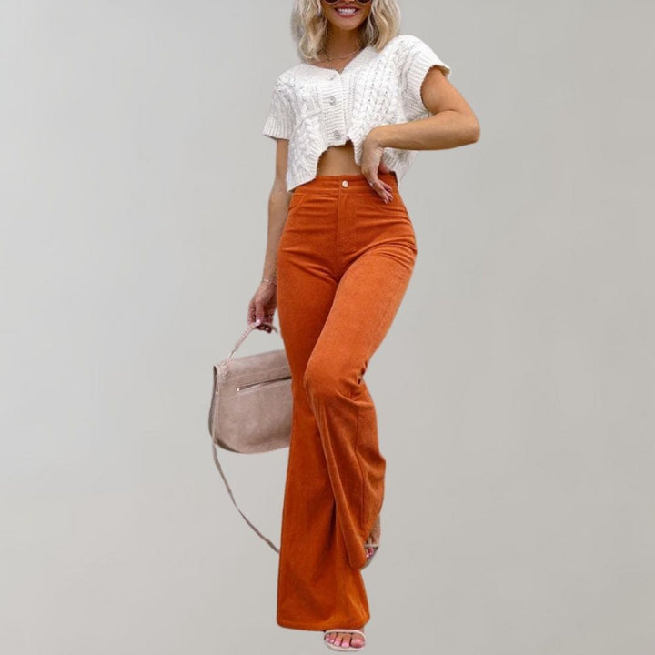 Vrouw draagt trendy oranje corduroy uitlopende broek met witte gebreide crop top en beige tas. Modieuze dameskleding, herfststijl.