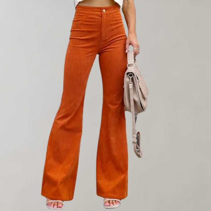 Oranje corduroy uitlopende broek voor dames, trendy en modieus, gecombineerd met een beige tas. Perfect voor casual en stijlvolle outfits.