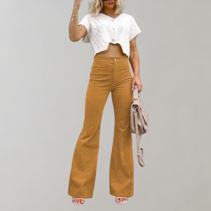 Vrouw in trendy bruine corduroy uitlopende broek en wit gebreid crop top, met beige tas. Modieuze dameskleding, herfststijl.