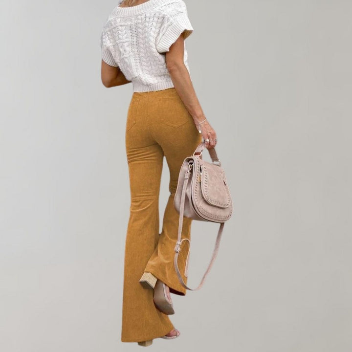 Trendy corduroy uitlopende broek in mosterdgeel, gecombineerd met een witte gebreide top en beige tas. Modieuze dameskleding, herfststijl.