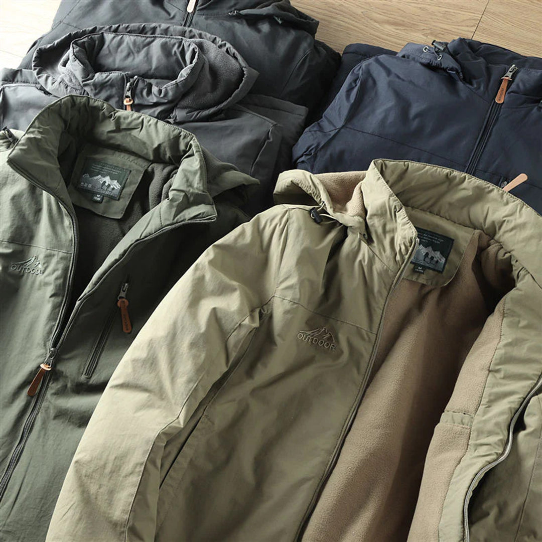 Verschillende kleuren outdoor jassen met capuchon, waaronder groen, zwart en blauw, op houten vloer. Ideaal voor wandelen en kamperen.