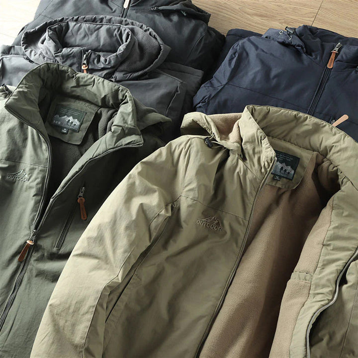 Verschillende kleuren outdoor jassen met capuchon, waaronder groen, zwart en blauw, op houten vloer. Ideaal voor wandelen en kamperen.